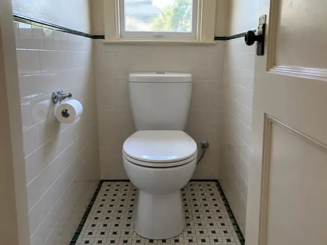 Clean white toilet in a tiled bathroom with a window and toilet roll holder in Roseville